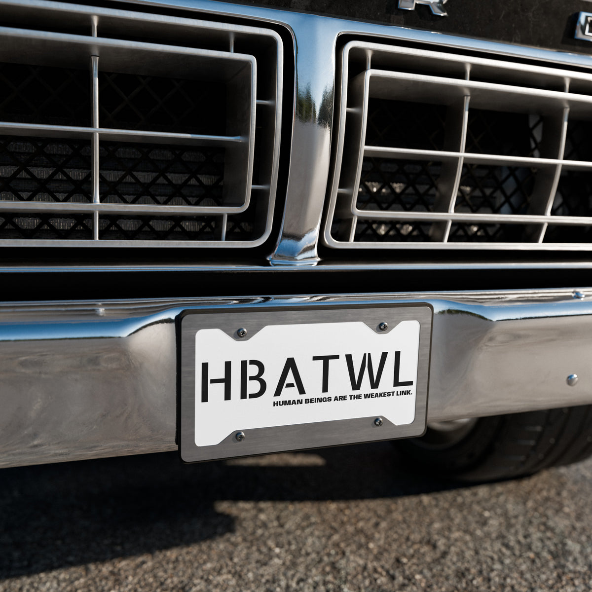 Front facing graphic vanity plate in color white, featuring the initialism 'HBATWL' and the statement 'HUMAN BEINGS ARE THE WEAKEST LINK.' in bold black print, affixed to a car's front bumper. From What Was Said (Statement Apparel + More).
