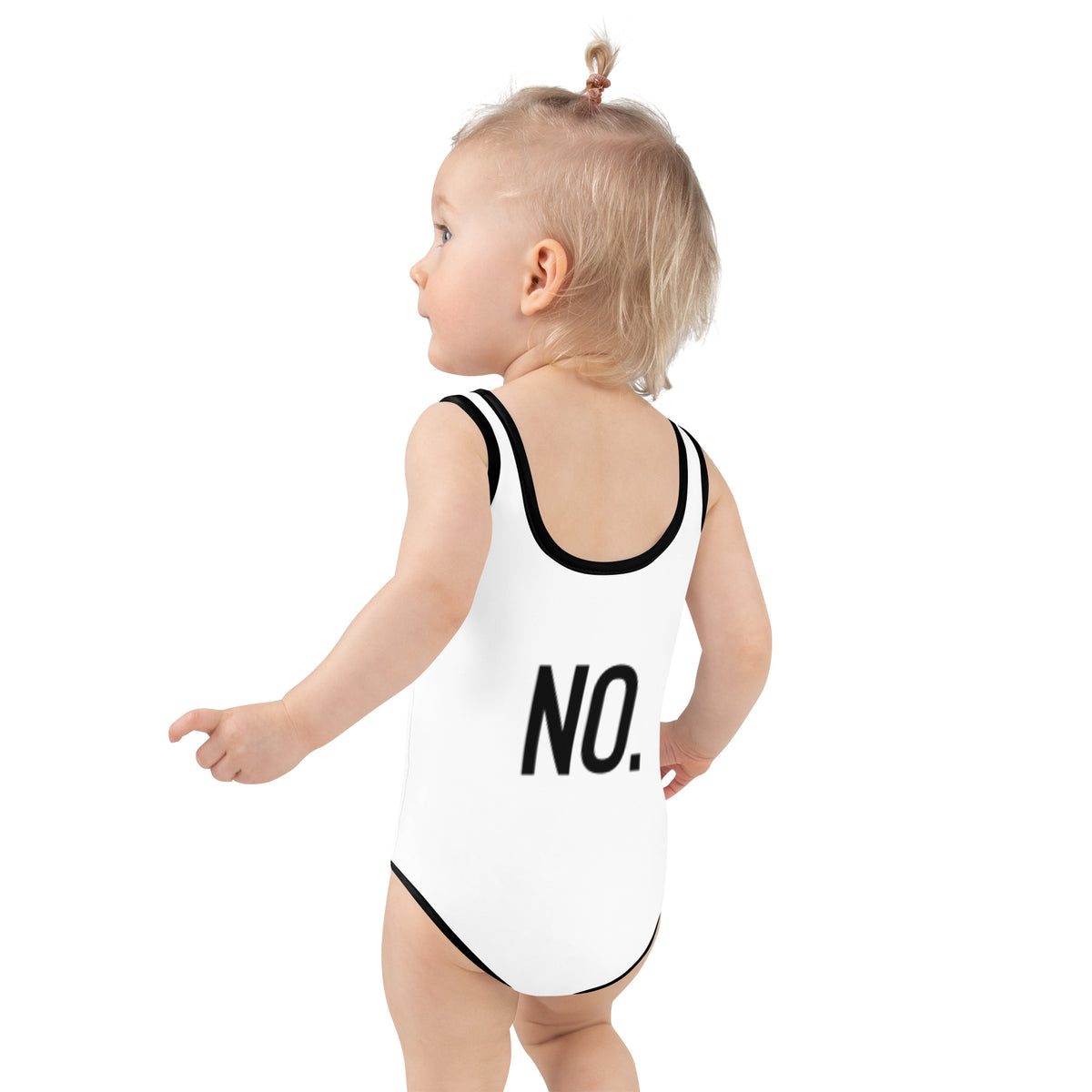 Model is wearing back facing kids graphic one-piece swimsuit in color white with black trim, featuring the statement 'NO.' in bold black print. From What Was Said (Statement Apparel + More).