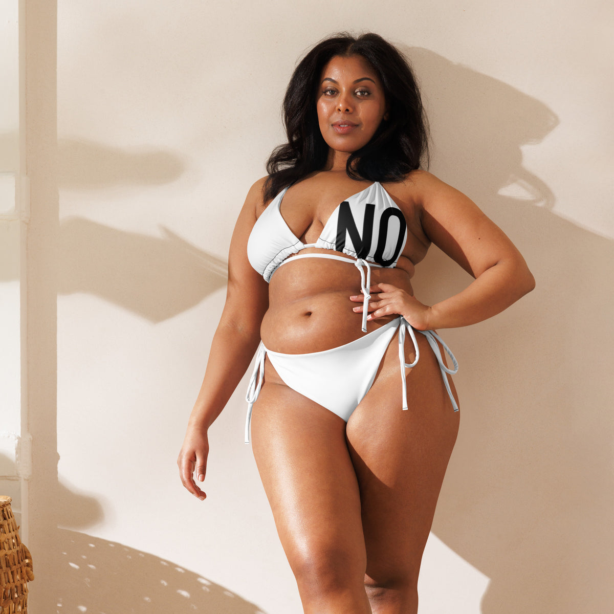 Model is wearing front facing graphic  string bikini swimsuit in color white, featuring the statement 'NO.' in bold black print on the breast cup of the bikini front top. From What Was Said (Statement Apparel + More).