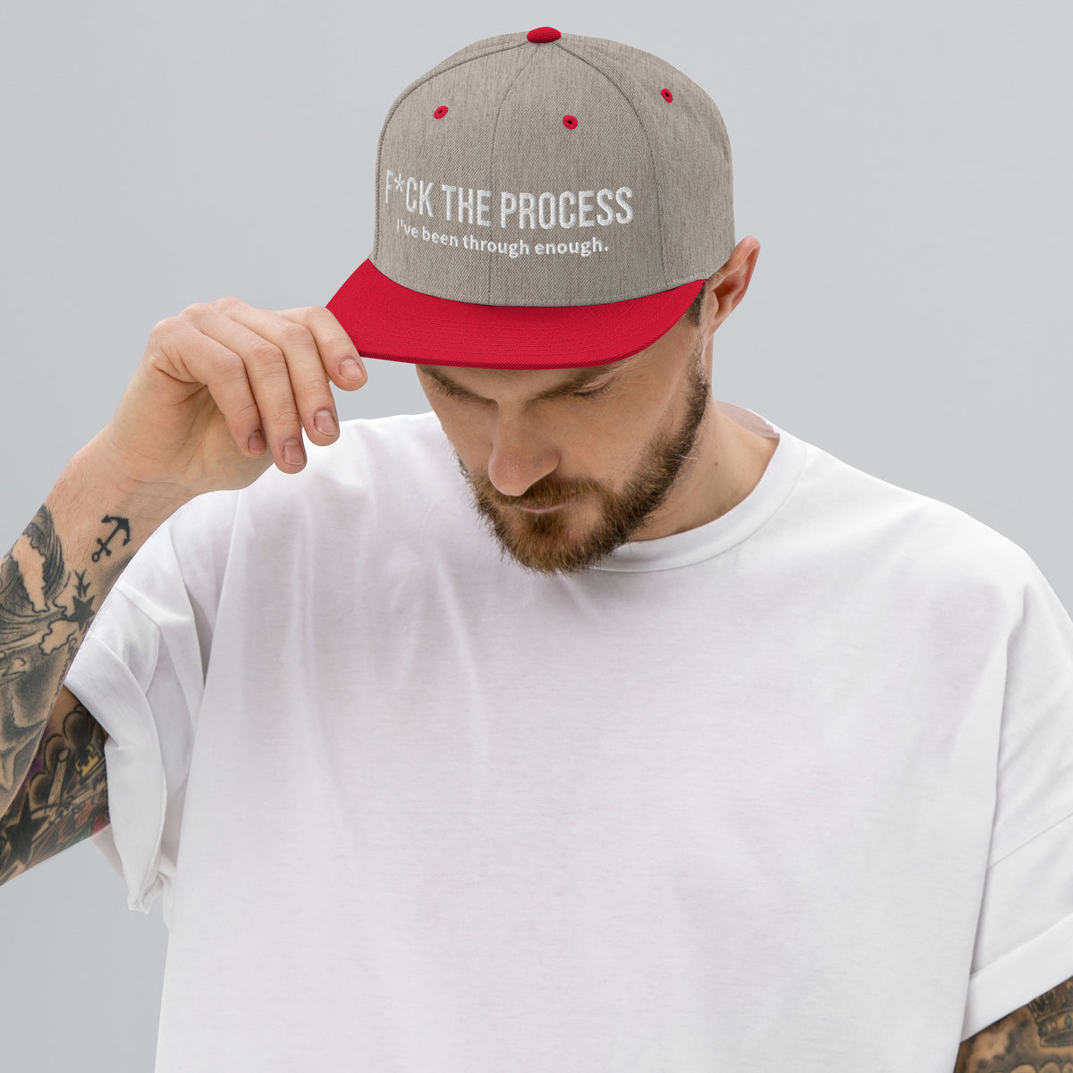Model is wearing front facing graphic snapback hat in color heather grey and red, featuring the statement 'FUCK THE PROCESS, I've Been Through Enough,' in bold white embroidery. From What Was Said (Statement Apparel + More).