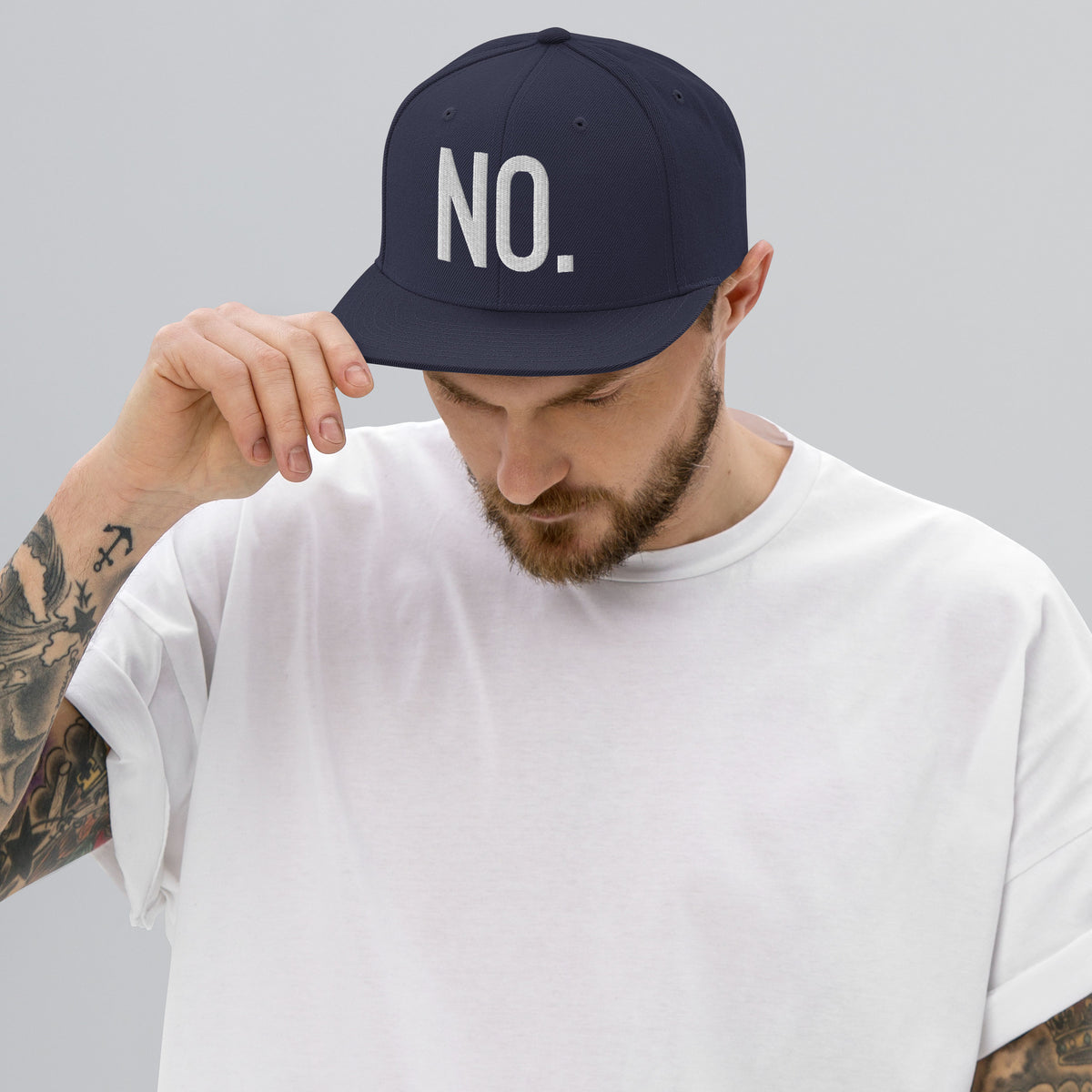 Model wearing front facing graphic snapback hat in color navy blue, featuring the statement 'NO.' in bold white embroidery. From What Was Said (Statement Apparel + More).