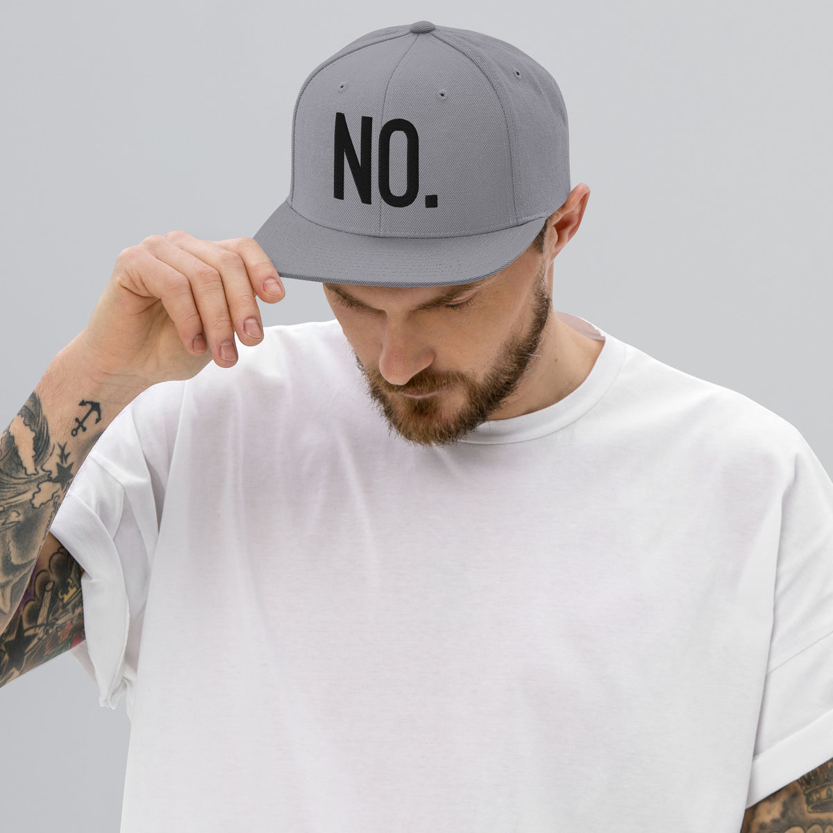 Model wearing front facing graphic snapback hat in color silver light grey, featuring the statement 'NO.' in bold black embroidery. From What Was Said (Statement Apparel + More).
