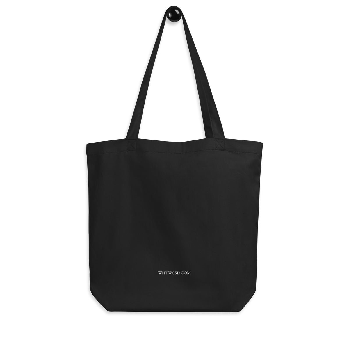 Back facing graphic eco tote bag in color black hanging from a hook against white background. Featuring brands website, WHTWSSD.COM, in bold white print, from What Was Said (Statement Apparel + More). 