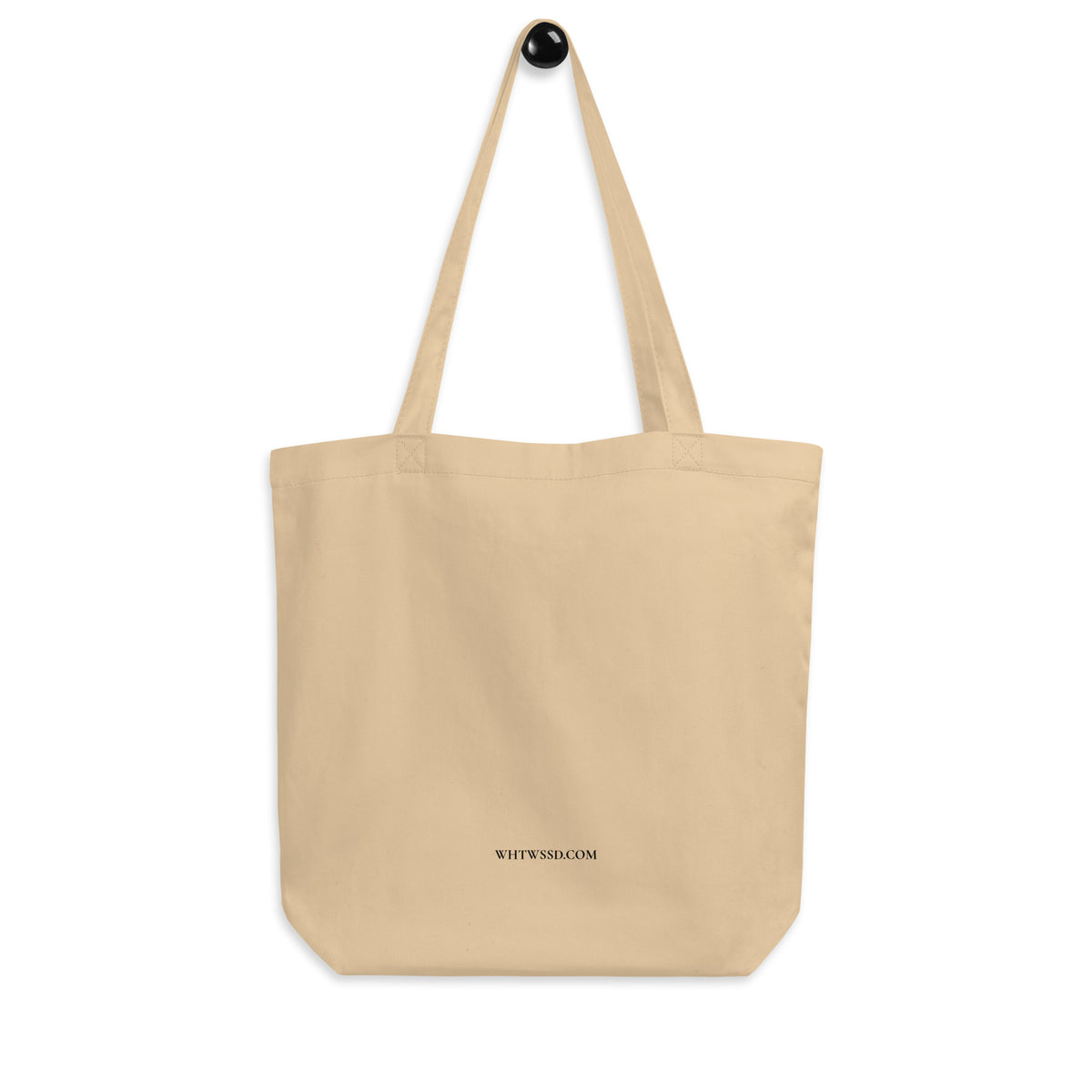 Back facing graphic eco tote bag in color oyster beige hanging from a hook against white background. Featuring brands website, WHTWSSD.COM, in bold black print, from What Was Said (Statement Apparel + More). 