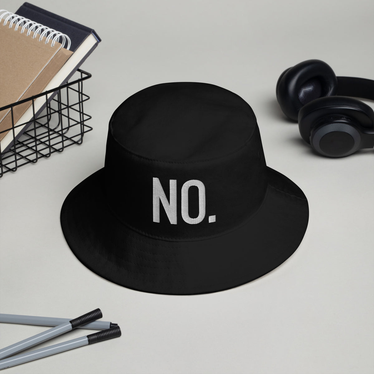 Front facing graphic bucket hat in color black on a desktop, featuring the statement 'NO.' in bold white embroidery. From What Was Said (Statement Apparel + More).