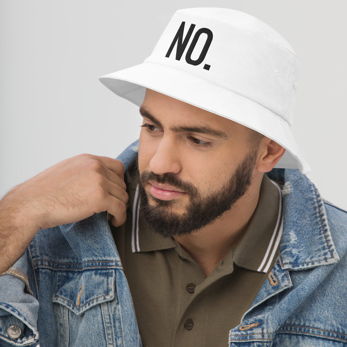 Model wearing left front facing graphic bucket hat in color white, featuring the statement 'NO.' in bold black embroidery. From What Was Said (Statement Apparel + More).