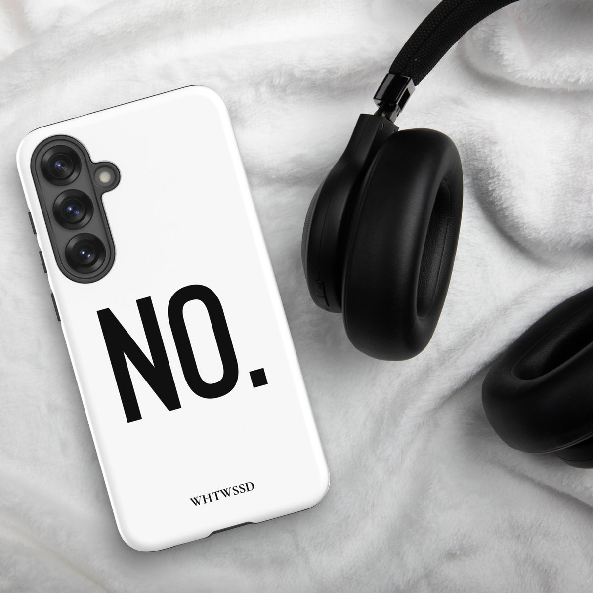 Front facing Samsung Galaxy S25 Plus graphic phone case in color white, on white faux fur background with headphones. Featuring the statement 'NO.' in bold black print on the phone case. From What Was Said (Statement Apparel + More). 