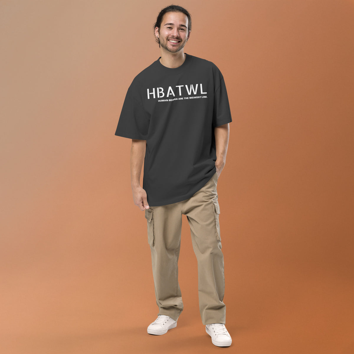 Model wearing front facing oversized fit graphic t-shirt in color faded black, featuring initialism, HBATWL, and statement 'HUMAN BEINGS ARE THE WEAKEST LINK', in bold white print. From What Was Said (Statement Apparel + More).