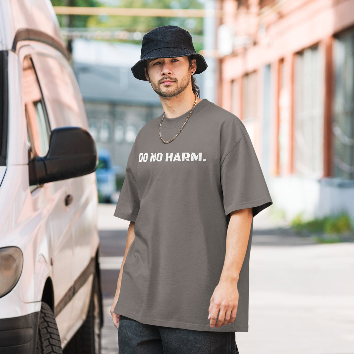 Model wearing front facing oversized fit graphic t-shirt in color faded grey, featuring statement that reads 'DO NO HARM', in bold white print. From What Was Said (Statement Apparel + More).
