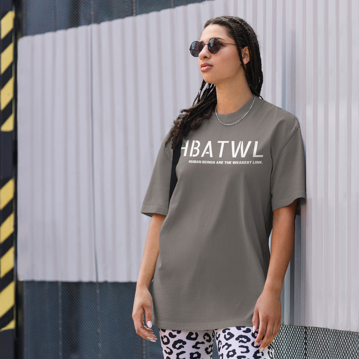 Model wearing front facing oversized fit graphic t-shirt in color faded grey, featuring initialism HBATWL, and statement 'HUMAN BEINGS ARE THE WEAKEST LINK', in bold white print. From What Was Said (Statement Apparel + More).