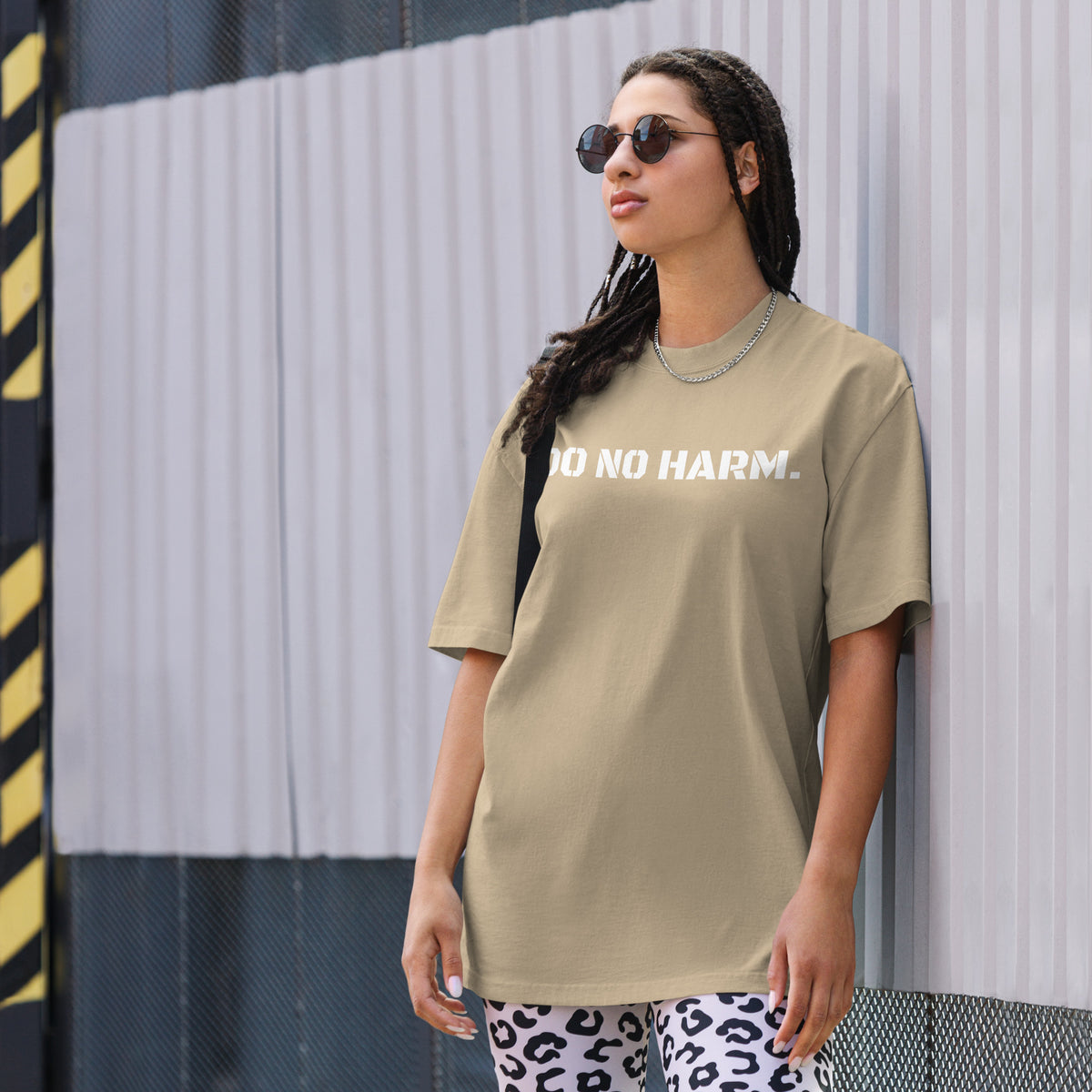 Model wearing front facing oversized fit graphic t-shirt in color faded khaki, featuring statement that reads 'DO NO HARM', in bold white print. From What Was Said (Statement Apparel + More).