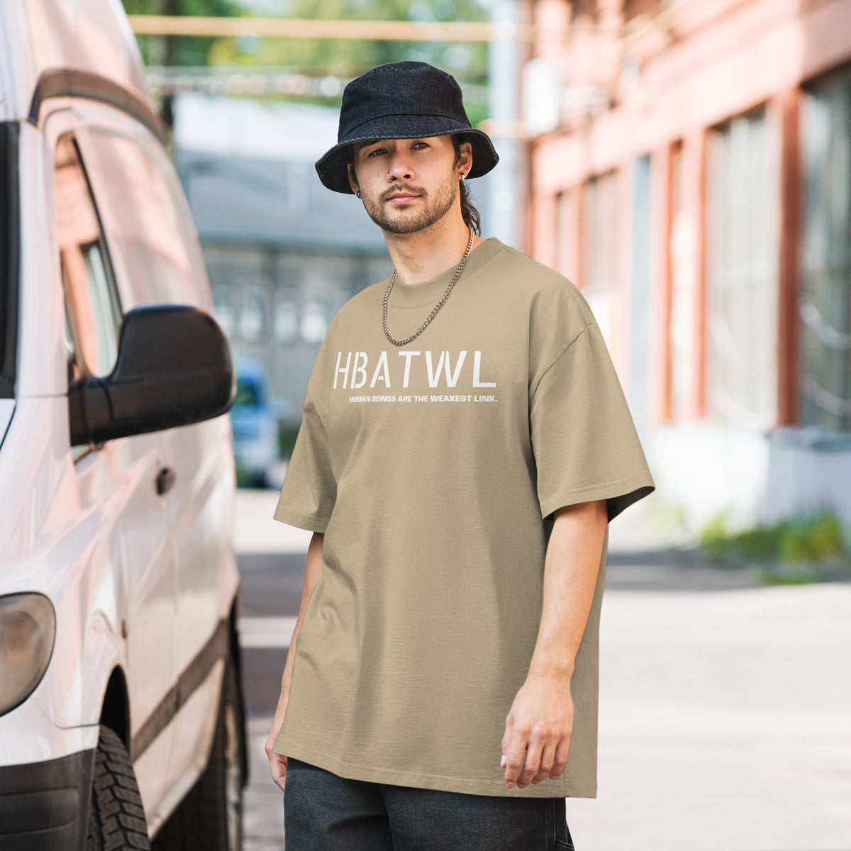 Model wearing front facing oversized fit graphic t-shirt in color faded khaki, featuring initialism HBATWL, and statement 'HUMAN BEINGS ARE THE WEAKEST LINK', in bold white print. From What Was Said (Statement Apparel + More).