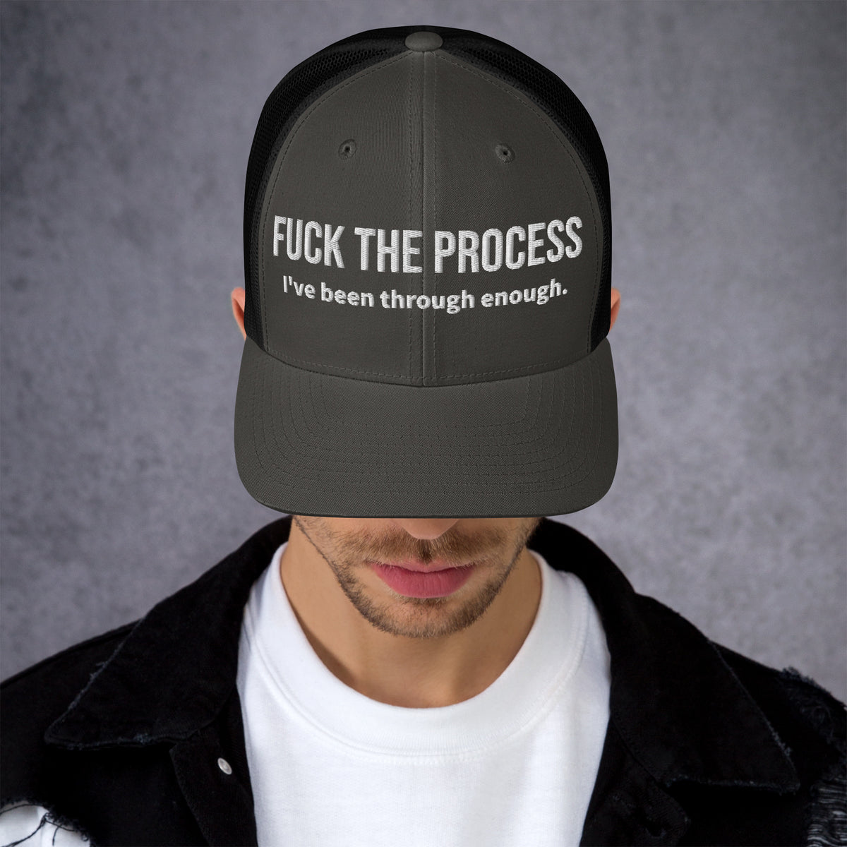 Model wearing front facing graphic trucker hat in color charcoal grey and black, featuring the statement 'FUCK THE PROCESS, I've Been Through Enough,' in bold white embroidery. From What Was Said (Statement Apparel + More).