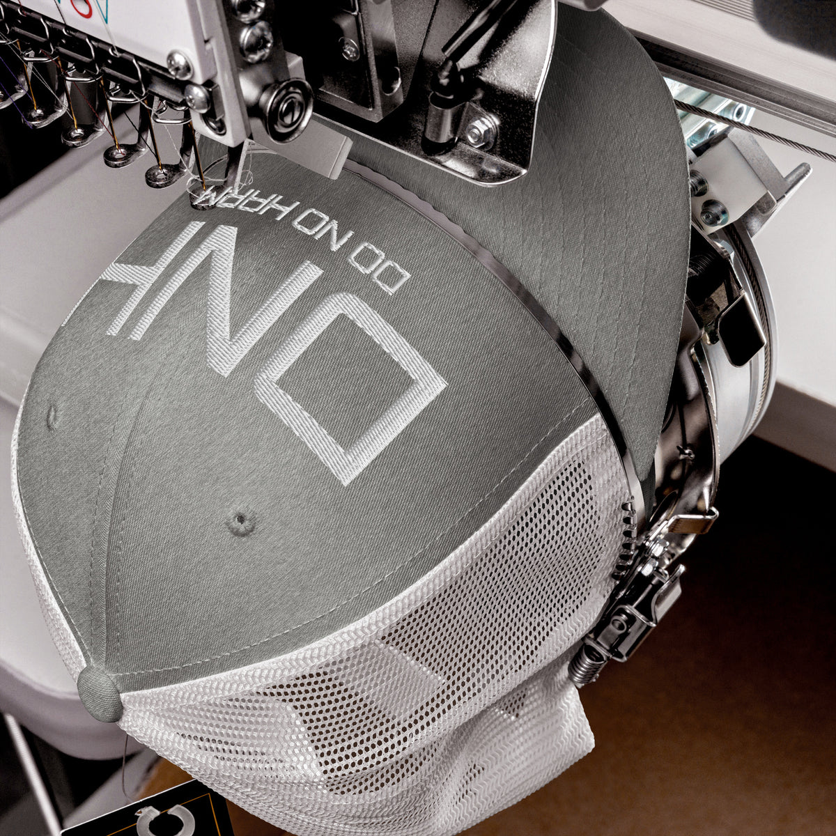 Product detail of embroidered stitching on front facing graphic trucker hat in color heather grey and white, featuring the initialism 'DNH', and the statement 'DO NO HARM,' in bold white embroidery. From What Was Said (Statement Apparel + More).