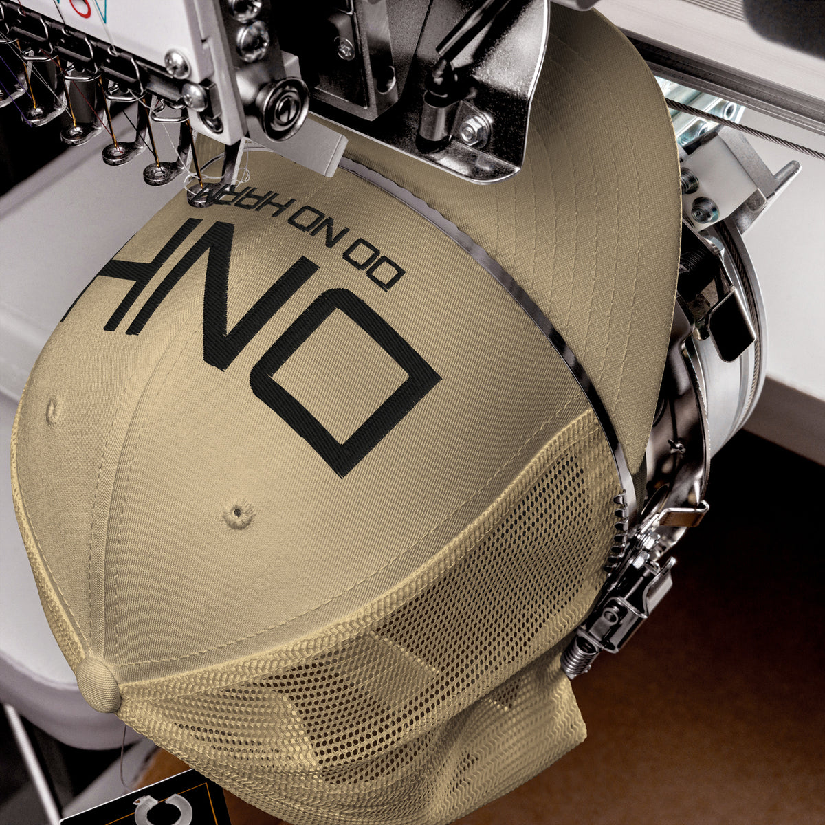 Product detail of embroidered stitching on front facing graphic trucker hat in color khaki, featuring the initialism 'DNH', and the statement 'DO NO HARM,' in bold black embroidery. From What Was Said (Statement Apparel + More).