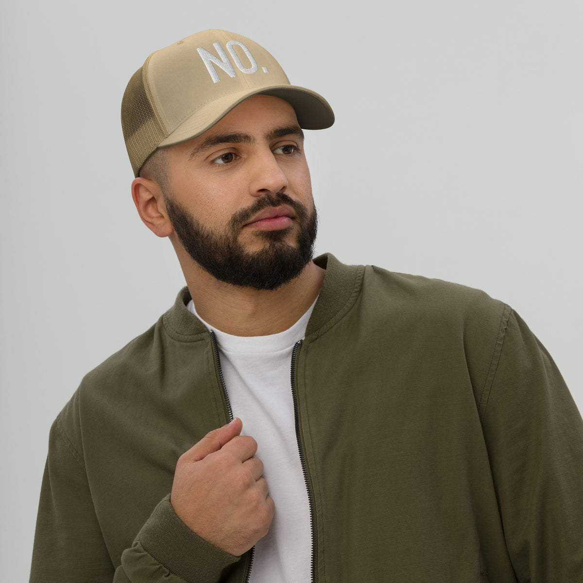Model is wearing front facing graphic trucker hat in color khaki, featuring the statement 'NO.' in bold white embroidery. From What Was Said (Statement Apparel + More).