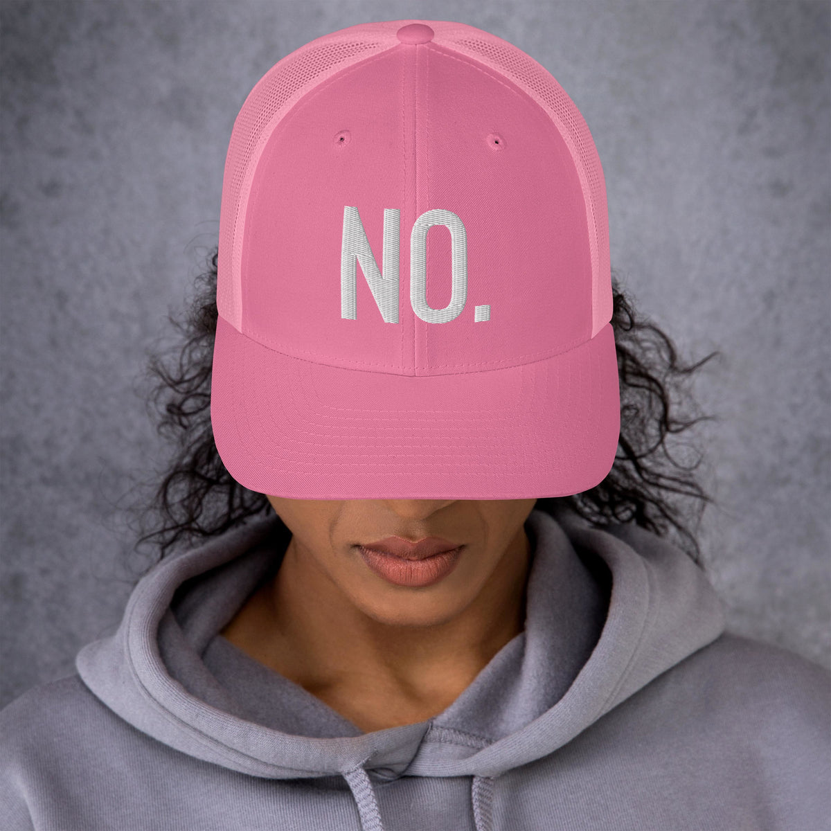 Model is wearing front facing graphic trucker hat in color pink, featuring the statement 'NO.' in bold white embroidery. From What Was Said (Statement Apparel + More).