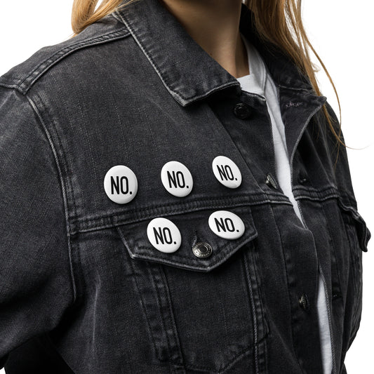 Model is wearing front facing graphic pin buttons, pinned to a jean jacket. Buttons are in color white and size 1.25 inches. Featuring the statement NO, in bold black print. From What Was Said (Statement Apparel + More). 