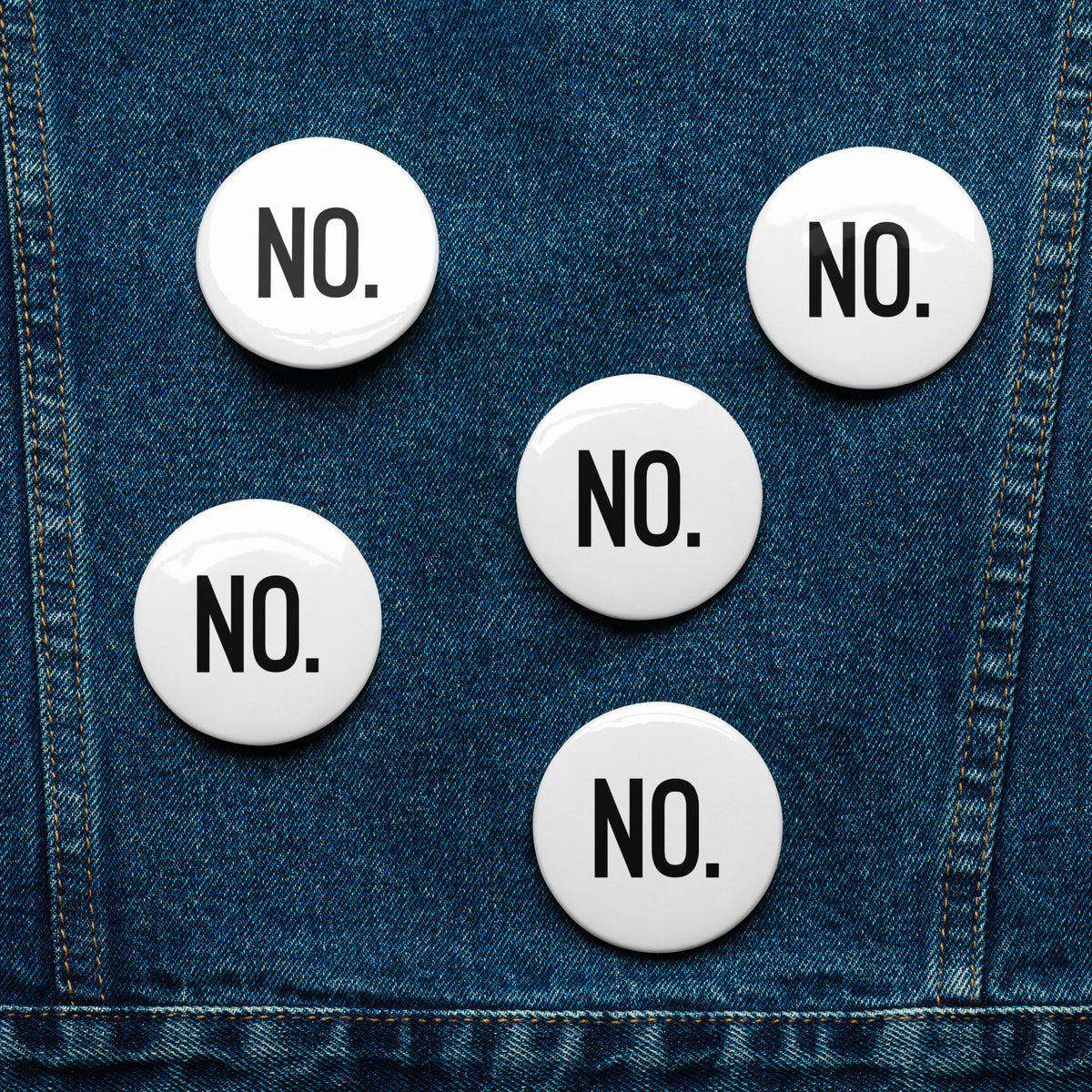 Front facing graphic pin buttons, pinned to a blue jean jacket. Buttons are in color white and size 2.25 inches. Featuring the statement NO in bold black print. From What Was Said (Statement Apparel + More). 