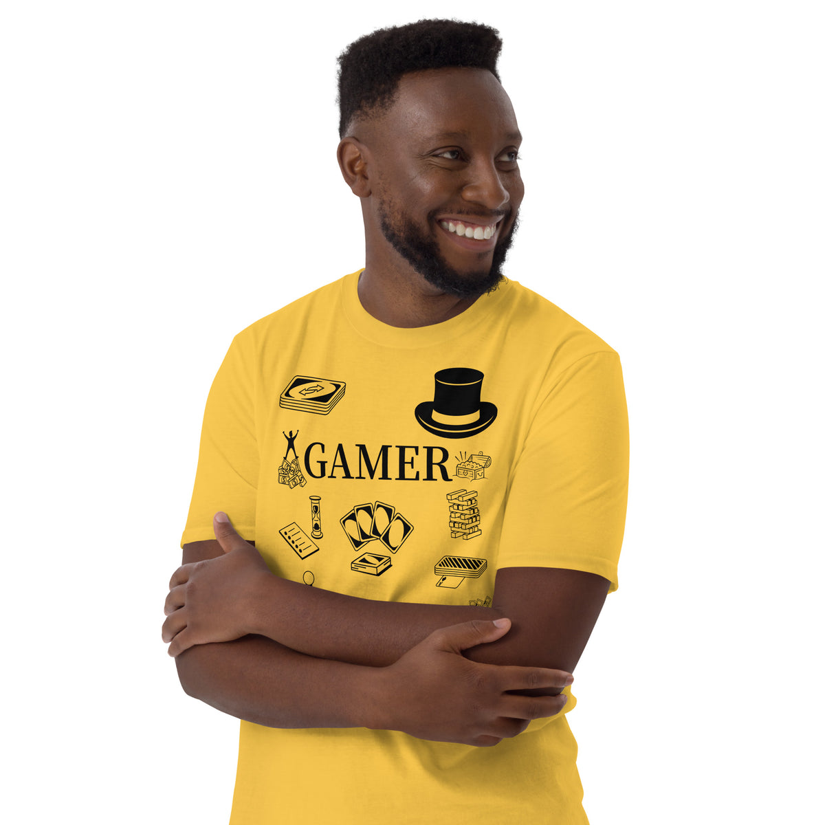Model is standing against a daisy yellow background wearing front facing graphic T-shirt in color daisy yellow, featuring printed image of various classic board game pieces and the word 'GAMER' in black print, from What Was Said (Statement Apparel + More). 