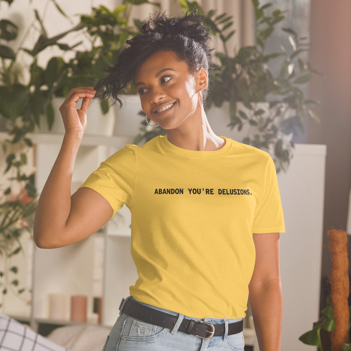 Model wearing front facing graphic t-shirt in color daisy yellow, featuring statement, 'ABANDON YOU'RE DELUSIONS', in bold black print. From What Was Said (Statement Apparel + More).