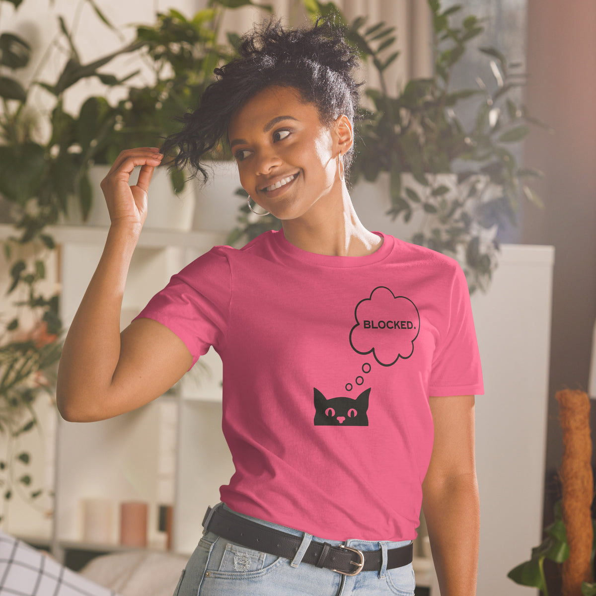 Model is wearing front facing graphic T-shirt in color heliconia pink, featuring printed image of cat with thought bubble, and the written word 'BLOCKED', inside the bubble in black print. From What Was Said (Statement Apparel + More). 