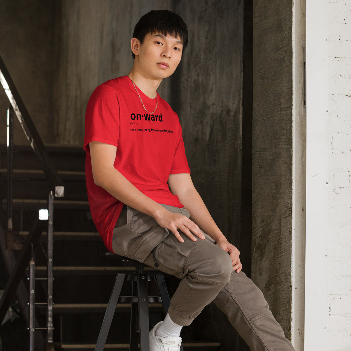 Model is wearing right front facing graphic t-shirt in color red, featuring written word 'ONWARD', with its definition in bold black print. From What Was Said (Statement Apparel + More).
