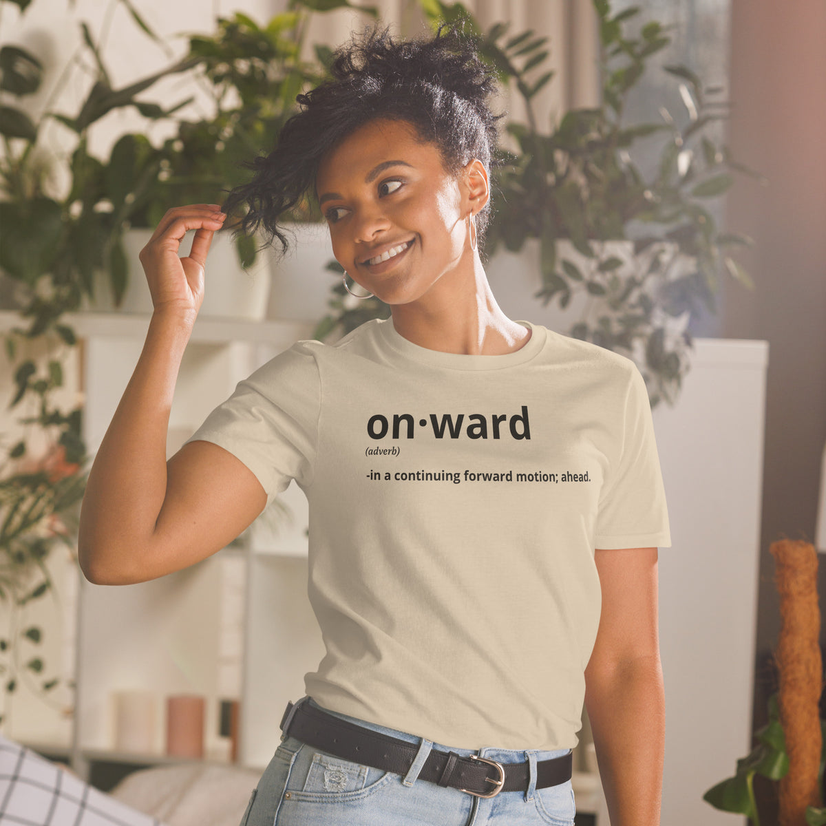 Model is wearing front facing graphic t-shirt in color sand, featuring written word 'ONWARD', with its definition in bold black print. From What Was Said (Statement Apparel + More).
