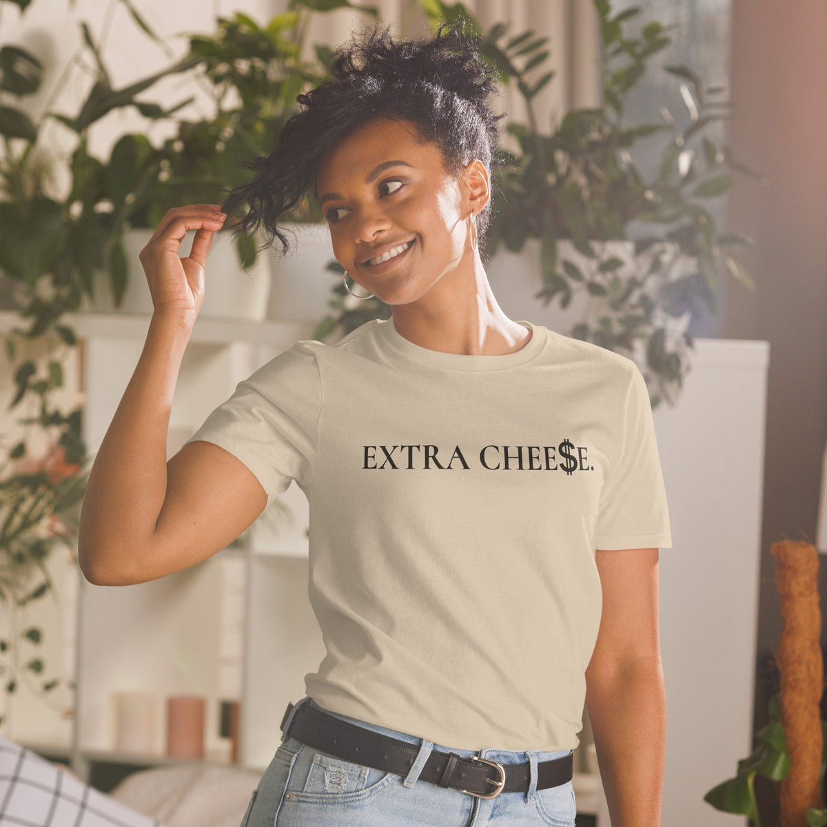 Model is wearing front facing graphic T-shirt in color sand, featuring statement 'EXTRA CHEESE', with dollar sign symbol in place of the letter S in the word cheese, in black print. From What Was Said (Statement Apparel + More).