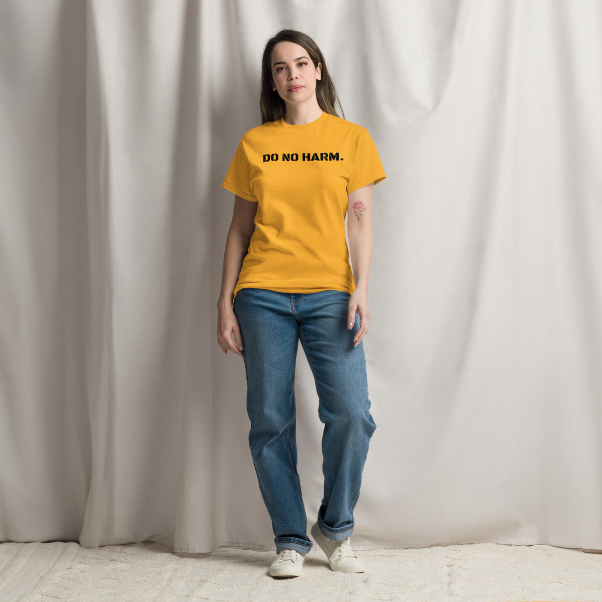 Model is wearing front facing graphic t-shirt in color gold yellow, featuring statement 'DO NO HARM', in bold black print. From What Was Said (Statement Apparel + More).